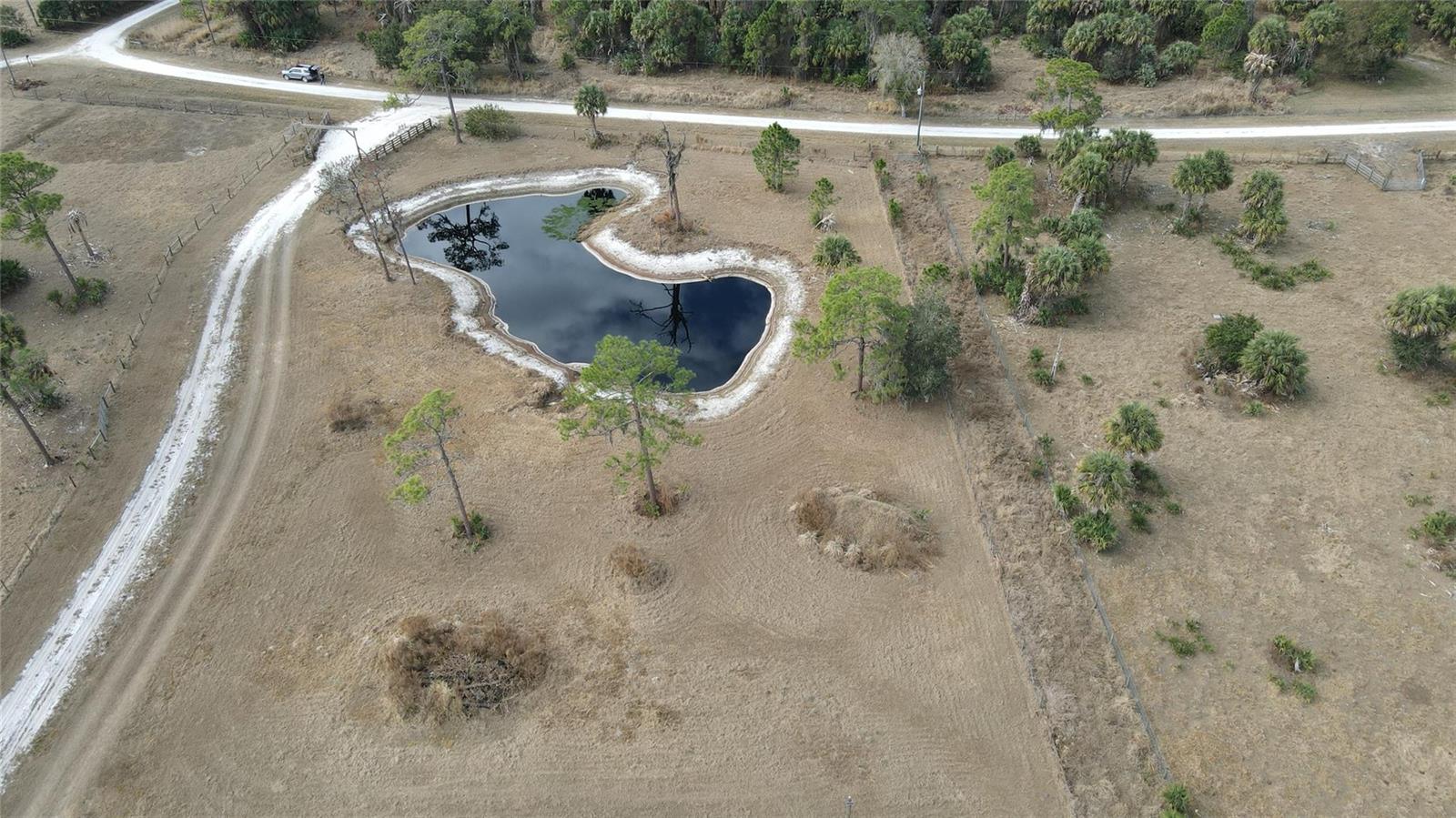 An aerial view shows a pond surrounded by dry grass and scattered trees on land — 4801 SW Wild Turkey Lane, Okeechobee FL 34974, OKEECHOBEE, FL