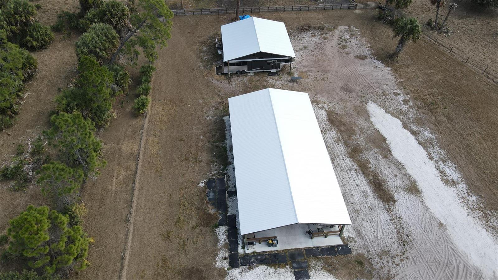 An aerial view shows two metal-roofed structures on a sandy lot with surrounding trees — 4801 SW Wild Turkey Lane, Okeechobee FL 34974, OKEECHOBEE, FL