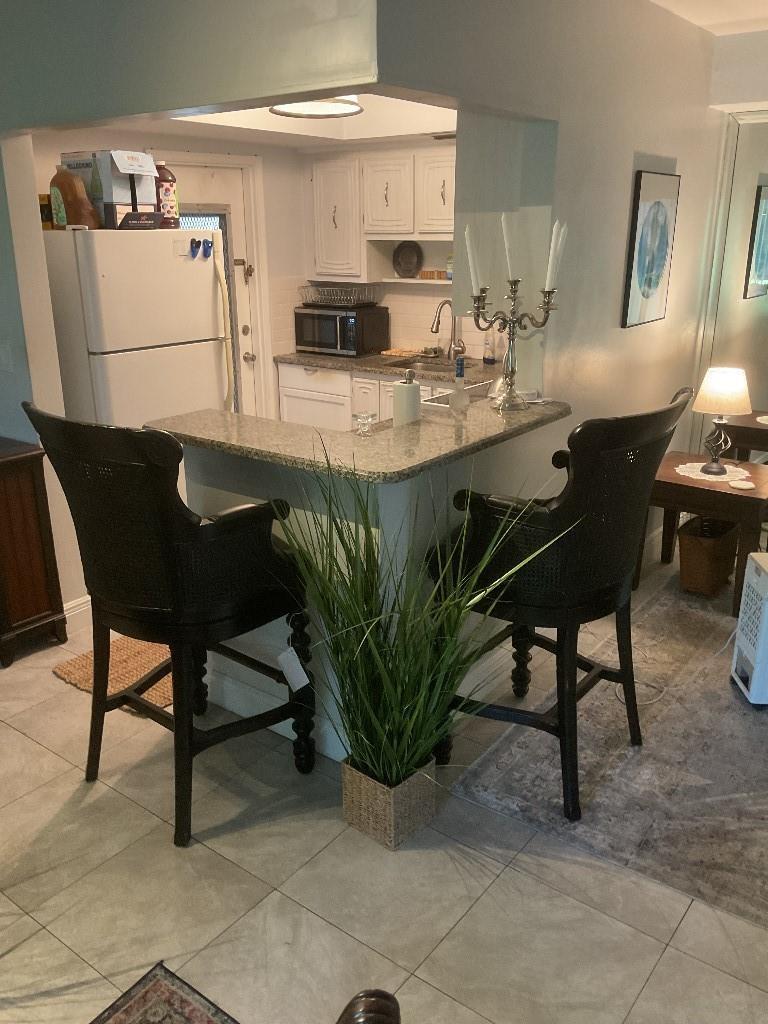 A kitchen with white cabinets, a granite breakfast bar, and two black bar stools — 100 SE 6th Avenue # 206, Pompano Beach FL 33060, POMPANO BEACH, FL