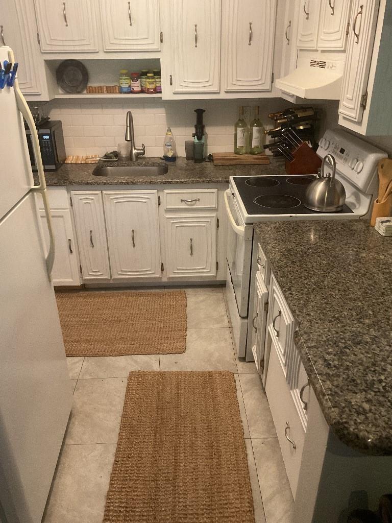 A galley kitchen features white cabinets, granite countertops, a white stove, and two jute rugs — 100 SE 6th Avenue # 206, Pompano Beach FL 33060, POMPANO BEACH, FL