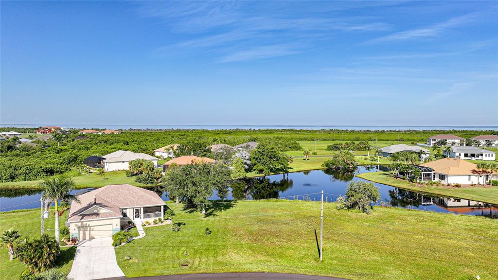 An aerial view shows a suburban house with a pool and pond near the coast — 17357 YOSEMITE COURT, PUNTA GORDA, FL