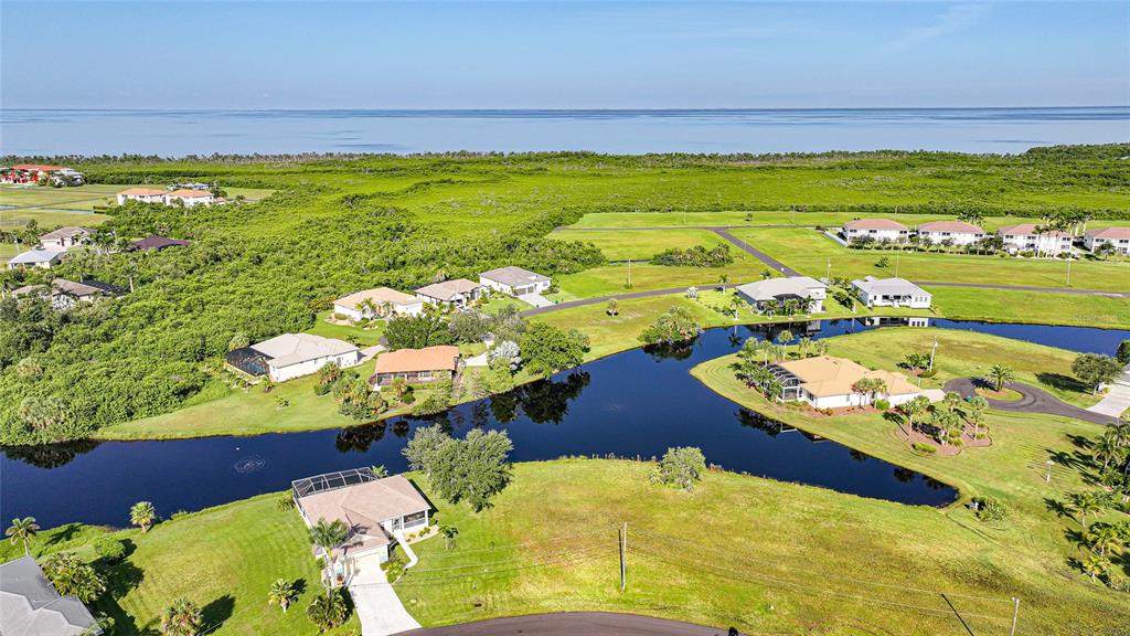 An aerial view shows several houses situated around a pond near a coastal landscape — 17357 YOSEMITE COURT, PUNTA GORDA, FL
