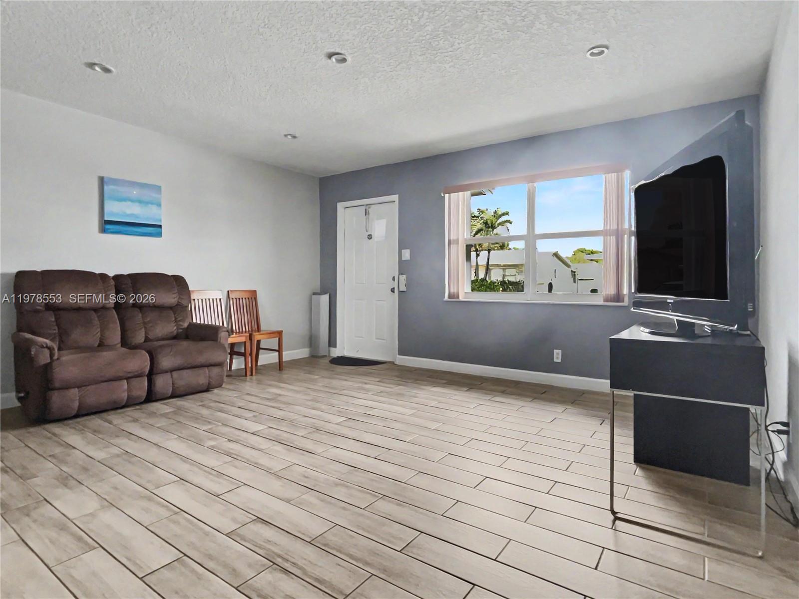 A living room features light wood-look tile flooring, a brown sofa, and a television stand — 6960 NW 11th Ct, Margate FL 33063, MARGATE, FL