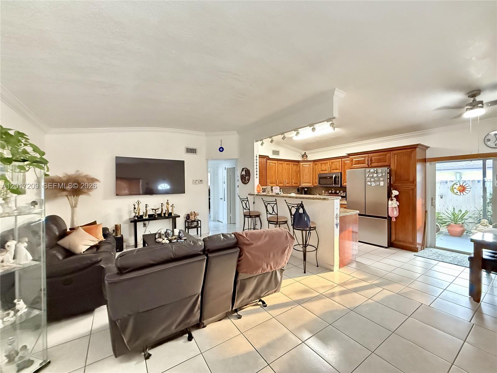 An open-concept living room and kitchen featuring tile floors, wood cabinetry, and a breakfast bar — 280 NE 173rd St, North Miami Beach FL 33162, NORTH MIAMI BEACH, FL