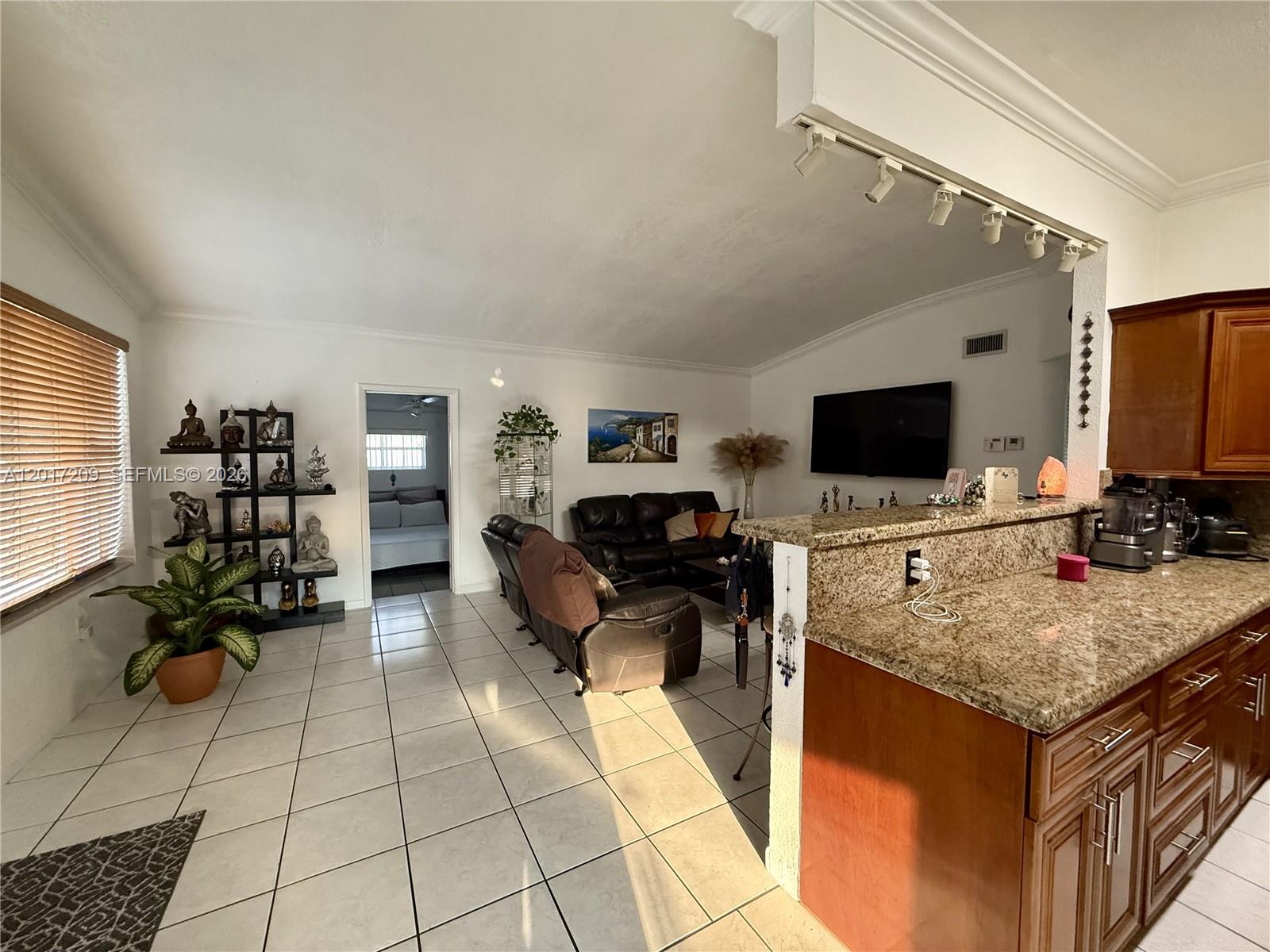 An open-concept living room features tile flooring, a granite-topped kitchen island, and dark leather furniture — 280 NE 173rd St, North Miami Beach FL 33162, NORTH MIAMI BEACH, FL
