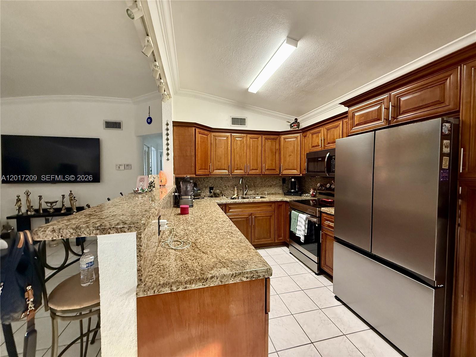 A kitchen features wood cabinets, granite countertops, stainless steel appliances, and a breakfast bar — 280 NE 173rd St, North Miami Beach FL 33162, NORTH MIAMI BEACH, FL