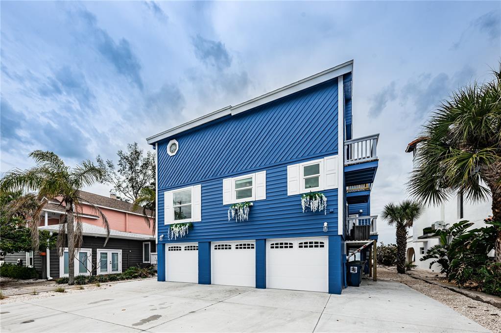 A three-story blue house with a three-car garage and white trim stands on a concrete lot — 8432 W GULF BOULEVARD UNIT Jellyfish, TREASURE ISLAND, FL