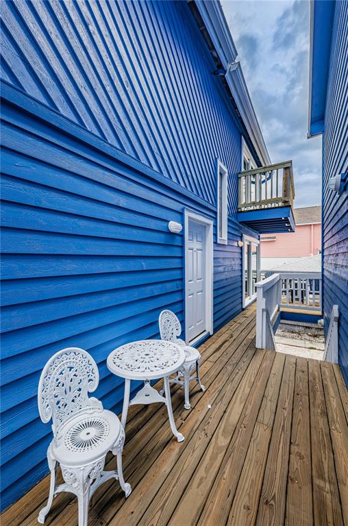 A wooden deck features a white metal bistro set against a bright blue house exterior — 8432 W GULF BOULEVARD UNIT Jellyfish, TREASURE ISLAND, FL