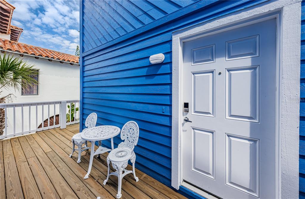 A blue-sided building exterior features a white door and a small patio with white furniture — 8432 W GULF BOULEVARD UNIT Jellyfish, TREASURE ISLAND, FL