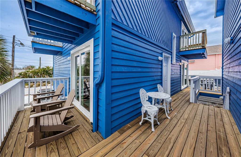 A blue wooden house exterior features a wooden deck with rocking chairs and bistro seating — 8432 W GULF BOULEVARD UNIT Jellyfish, TREASURE ISLAND, FL
