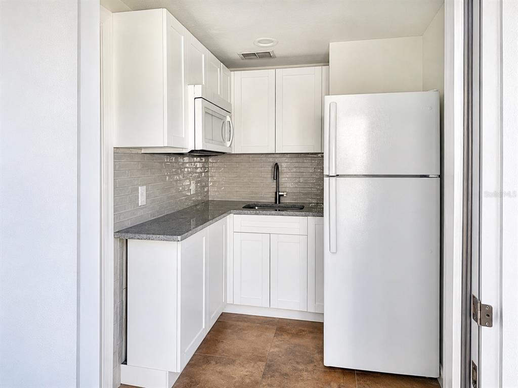 A small kitchen features white cabinets, gray granite countertops, a tiled backsplash, and white appliances — 2232 SELKIRK STREET, VALRICO, FL