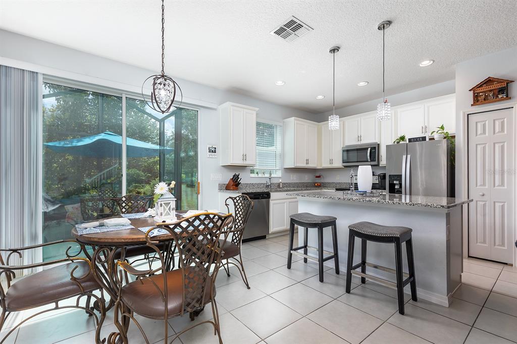 A kitchen and dining area with white cabinets, granite countertops, stainless appliances, and tile flooring — 4848 CLIVEDEN LOOP, SANFORD, FL