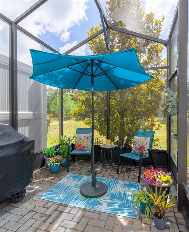 A screened-in patio features a blue umbrella, two chairs, and potted plants on brick pavers — 4848 CLIVEDEN LOOP, SANFORD, FL