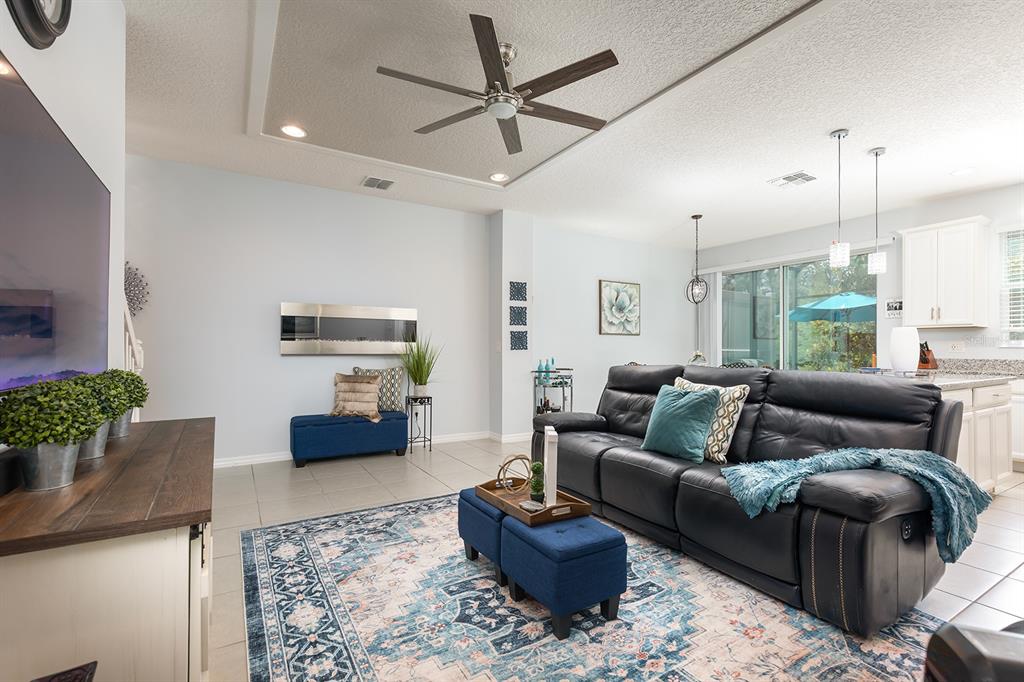 A living room with a black leather sofa, blue ottomans, and a wall-mounted fireplace — 4848 CLIVEDEN LOOP, SANFORD, FL