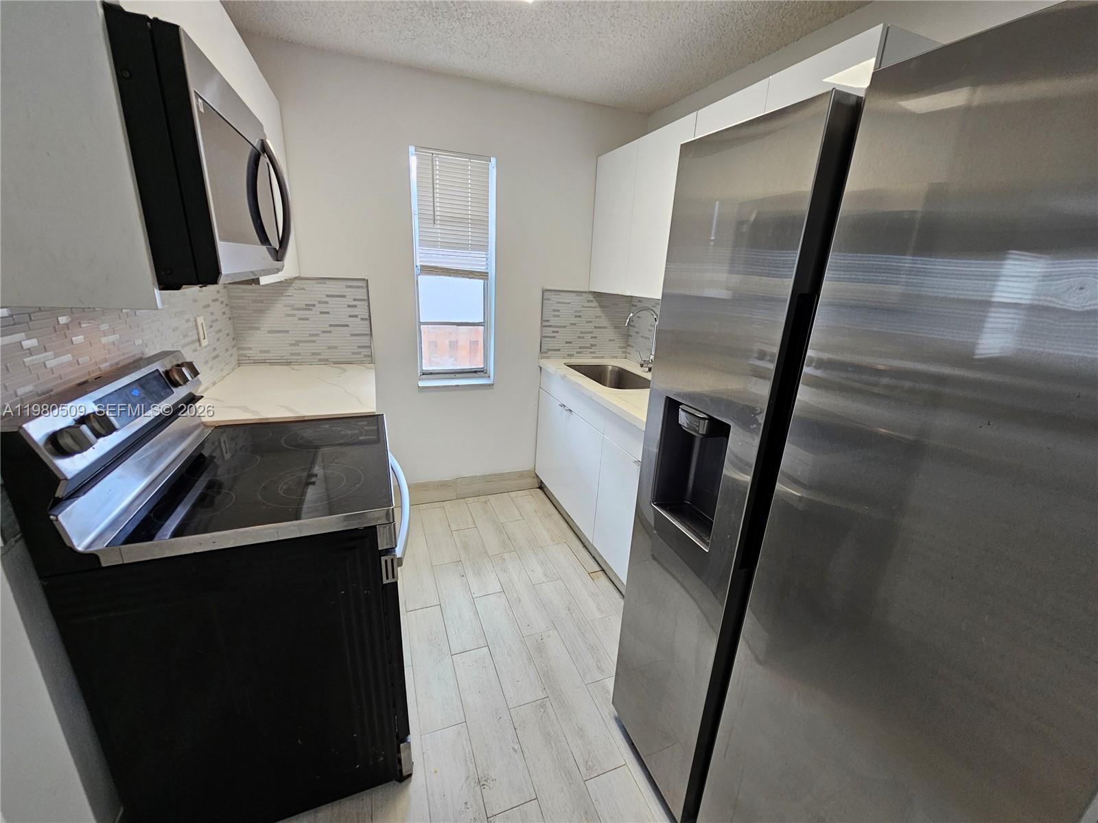 A galley kitchen features stainless steel appliances, white cabinetry, and light-colored wood-look tile flooring — 4621 SW 33rd Ave # 1, Dania Beach FL 33312, DANIA BEACH, FL