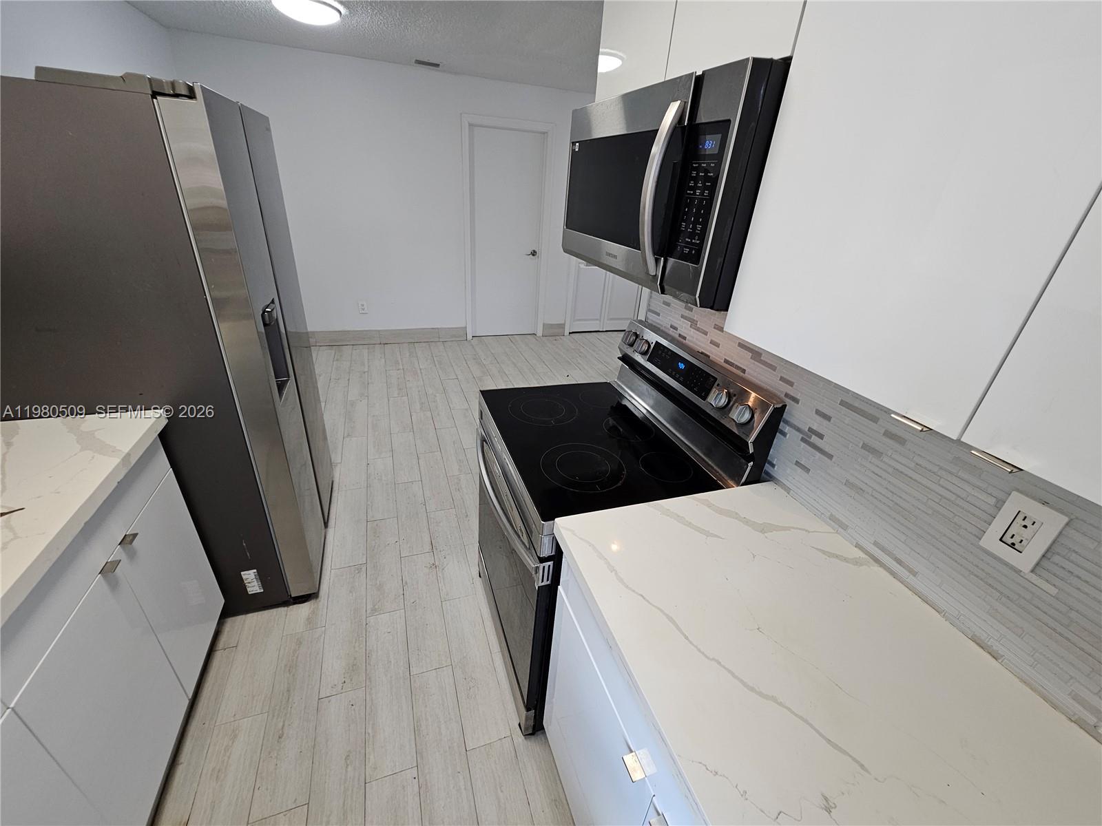 A modern kitchen features white cabinets, stainless steel appliances, and light-colored wood-look tile flooring — 4621 SW 33rd Ave # 1, Dania Beach FL 33312, DANIA BEACH, FL