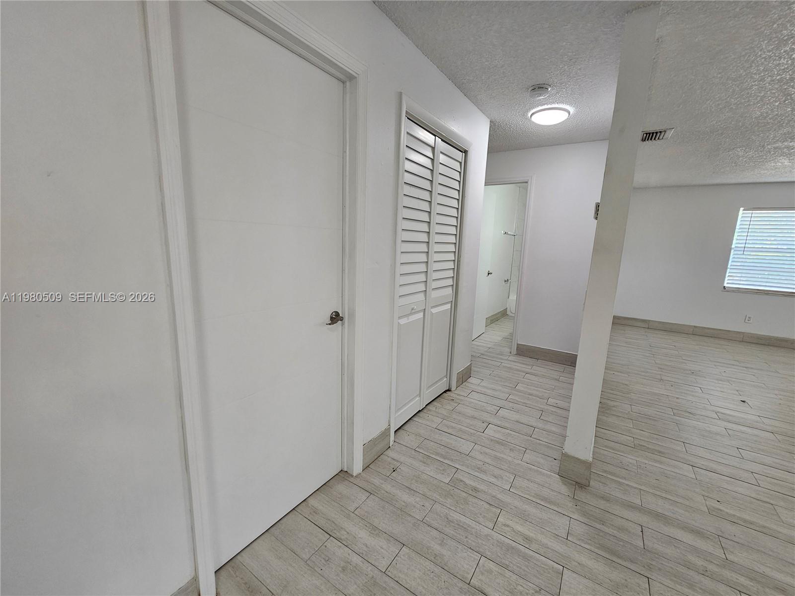 A hallway with white walls, light wood-look tile flooring, and several closed doors — 4621 SW 33rd Ave # 1, Dania Beach FL 33312, DANIA BEACH, FL