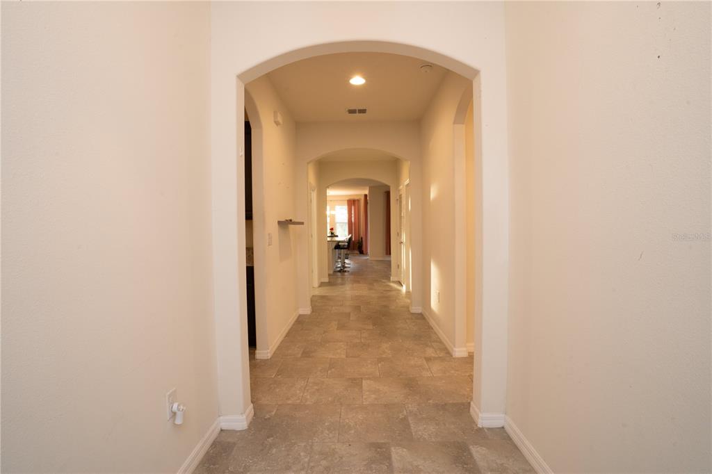 A long, tiled hallway with arched entryways leads toward a kitchen area — 4004 PRIMA LAGO CIRCLE, LAKELAND, FL