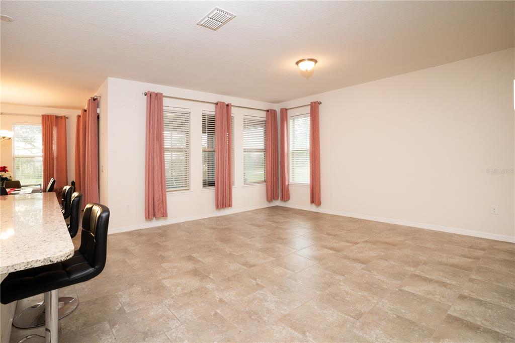 An open-concept living area features tile flooring, a granite kitchen island, and pink window curtains — 4004 PRIMA LAGO CIRCLE, LAKELAND, FL