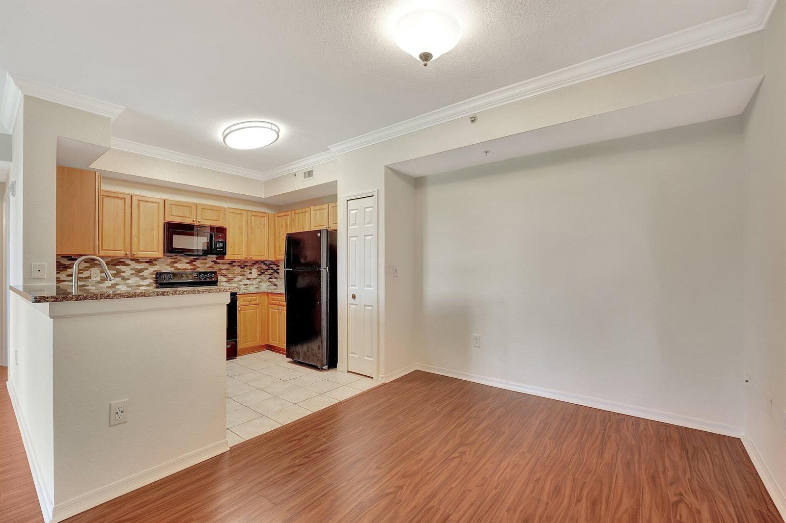 This kitchen features light wood cabinets, black appliances, a tiled floor, and an adjacent area — 15055 Michelangelo Boulevard # 208, Delray Beach FL 33446, DELRAY BEACH, FL