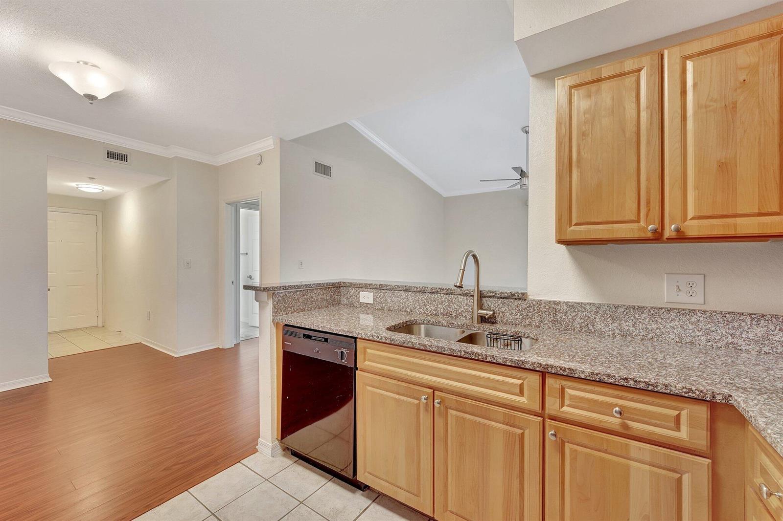 A kitchen with light wood cabinets, granite countertops, and a dishwasher, overlooking a living area — 15055 Michelangelo Boulevard # 208, Delray Beach FL 33446, DELRAY BEACH, FL