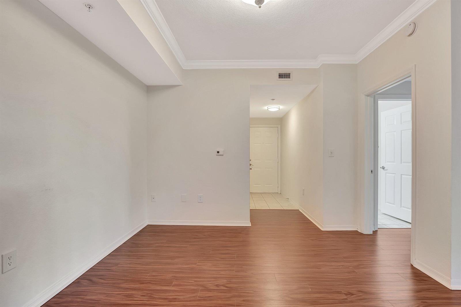 An empty room with wood-look flooring, white walls, and a doorway leading to an entryway — 15055 Michelangelo Boulevard # 208, Delray Beach FL 33446, DELRAY BEACH, FL