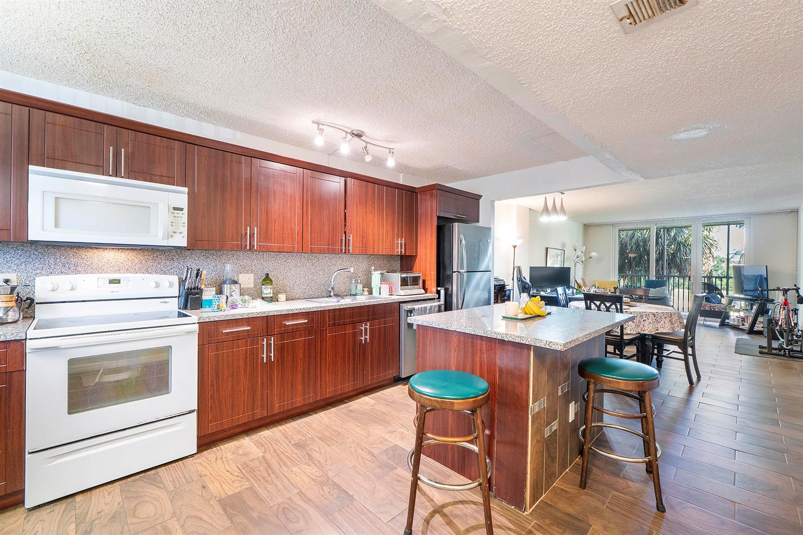 A kitchen features wood cabinets, granite countertops, a central island with stools, and tile flooring — 250 Jacaranda Drive # 308, Plantation FL 33324, PLANTATION, FL