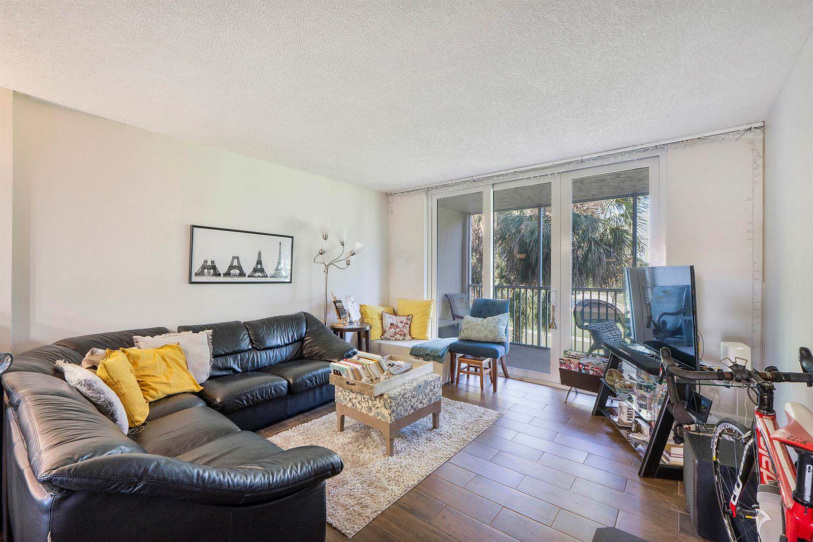 A living room features a black leather sectional, tile flooring, and sliding glass balcony doors — 250 Jacaranda Drive # 308, Plantation FL 33324, PLANTATION, FL