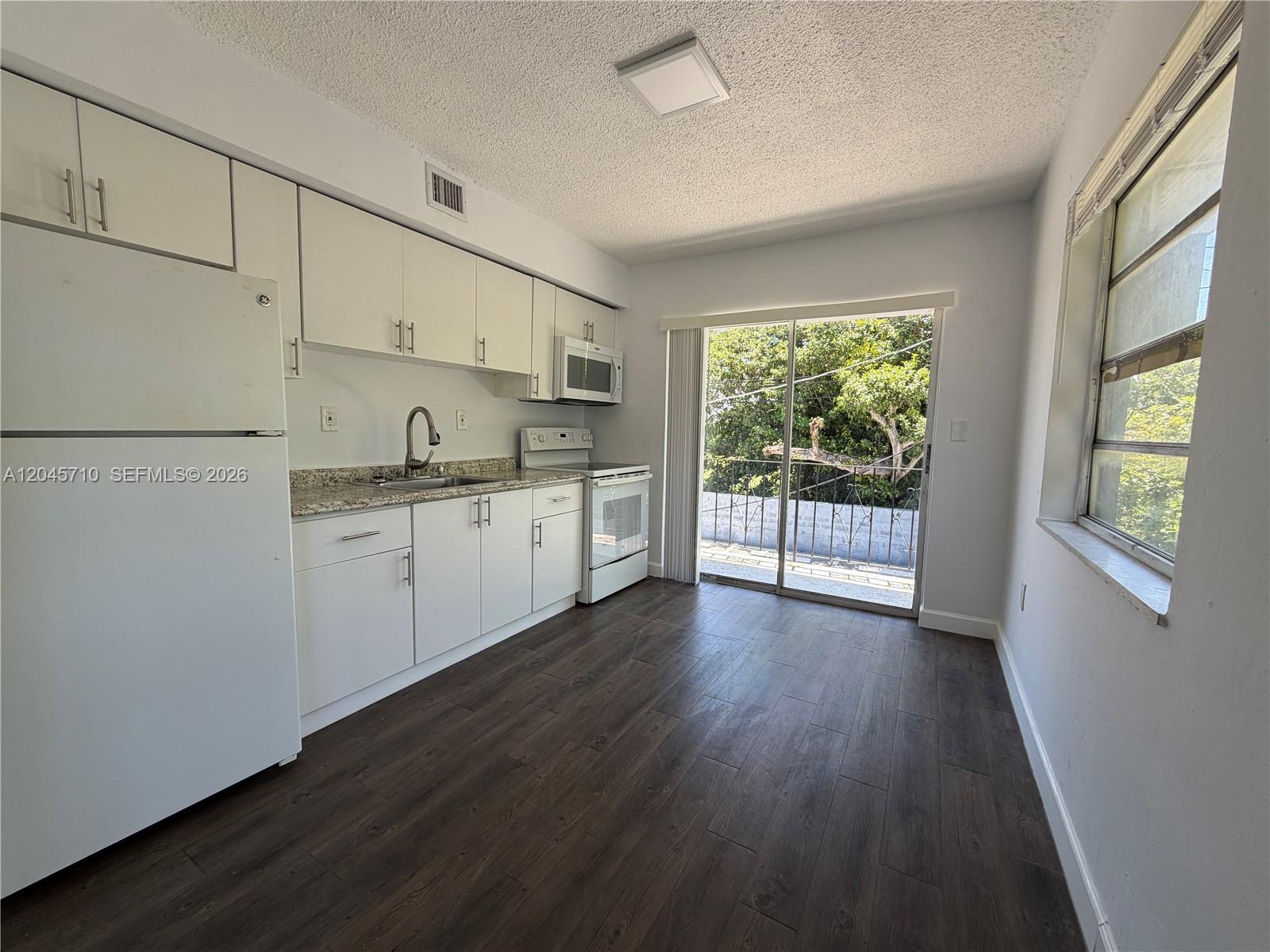 A kitchen with white cabinets, granite countertops, stainless steel appliances, and a sliding glass door — 5954 NE 4th Ct # 6, Miami FL 33137, MIAMI, FL