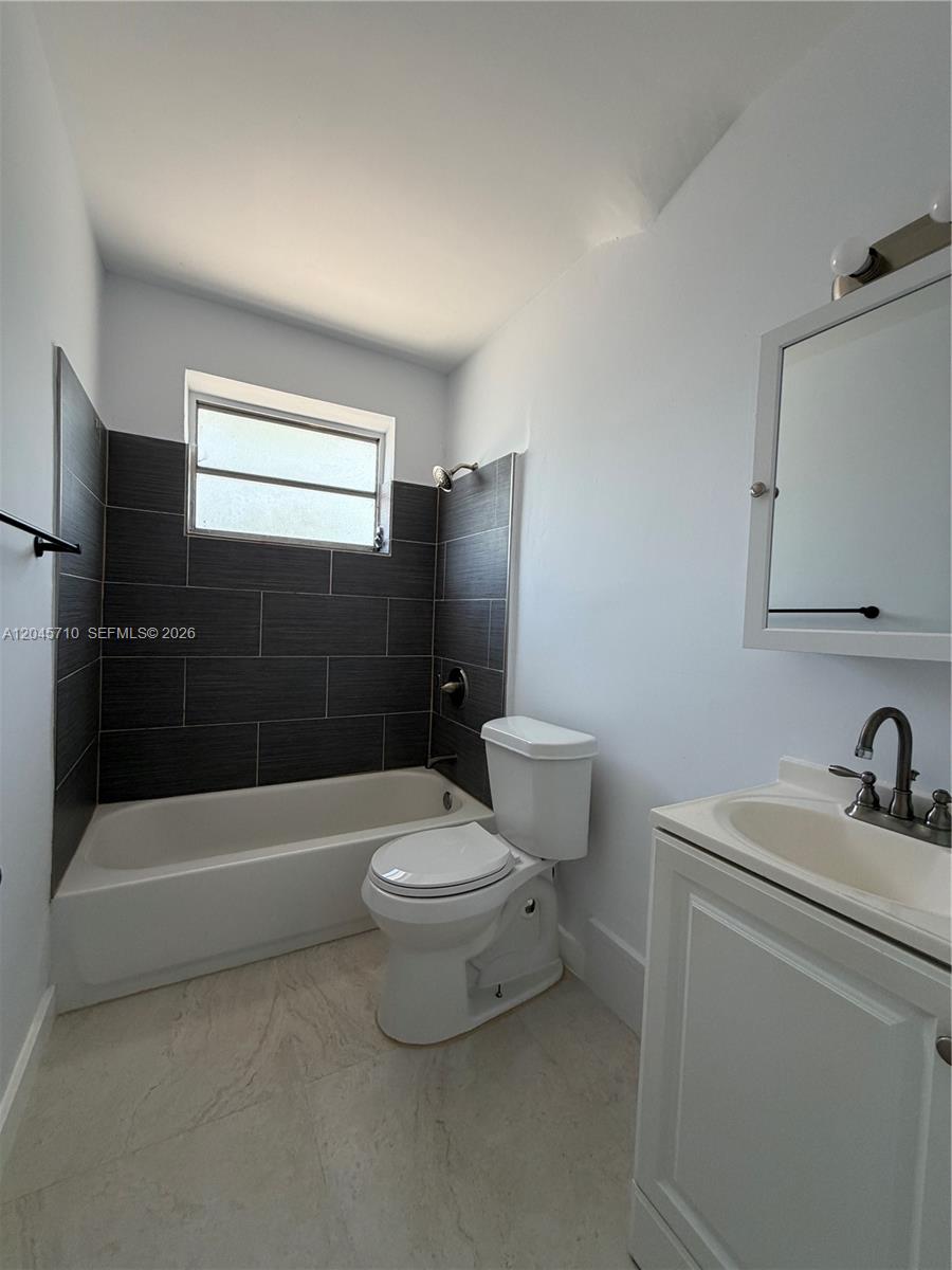 A bathroom features a white tub with dark gray tile walls, a toilet, and a vanity — 5954 NE 4th Ct # 6, Miami FL 33137, MIAMI, FL