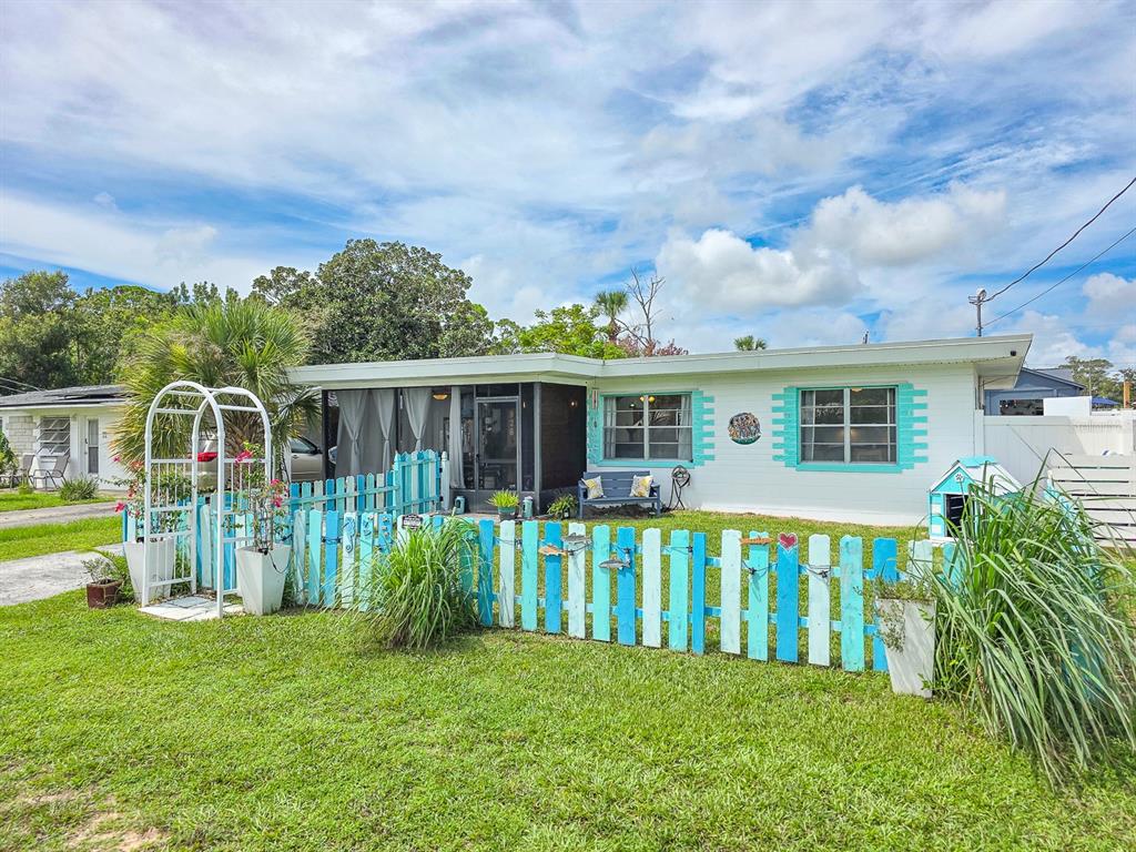 A single-story house with a white exterior, turquoise trim, and a colorful picket fence — 926 FERNALD STREET, EDGEWATER, FL