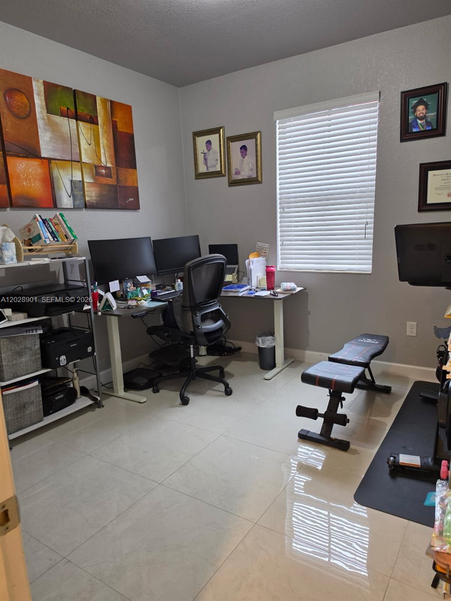 A home office features a desk with two monitors, a chair, and a workout bench — HIALEAH, FL