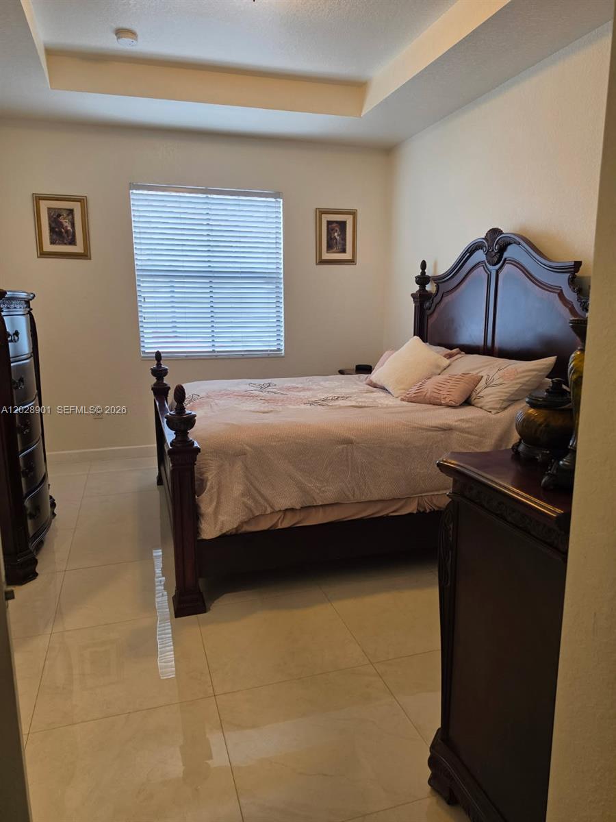 A bedroom features a dark wood bed frame, tiled flooring, and a tray ceiling — HIALEAH, FL