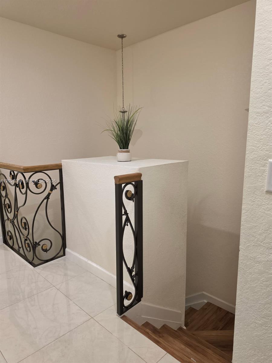 A staircase with decorative metal railings leads down from a tiled landing with a plant — HIALEAH, FL