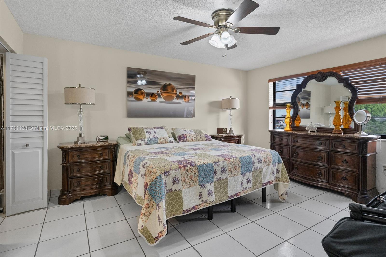 A bedroom features a patchwork quilt bed, dark wood furniture, and white tile flooring — 605 NW 72nd Ave # 406, Miami FL 33126, MIAMI, FL