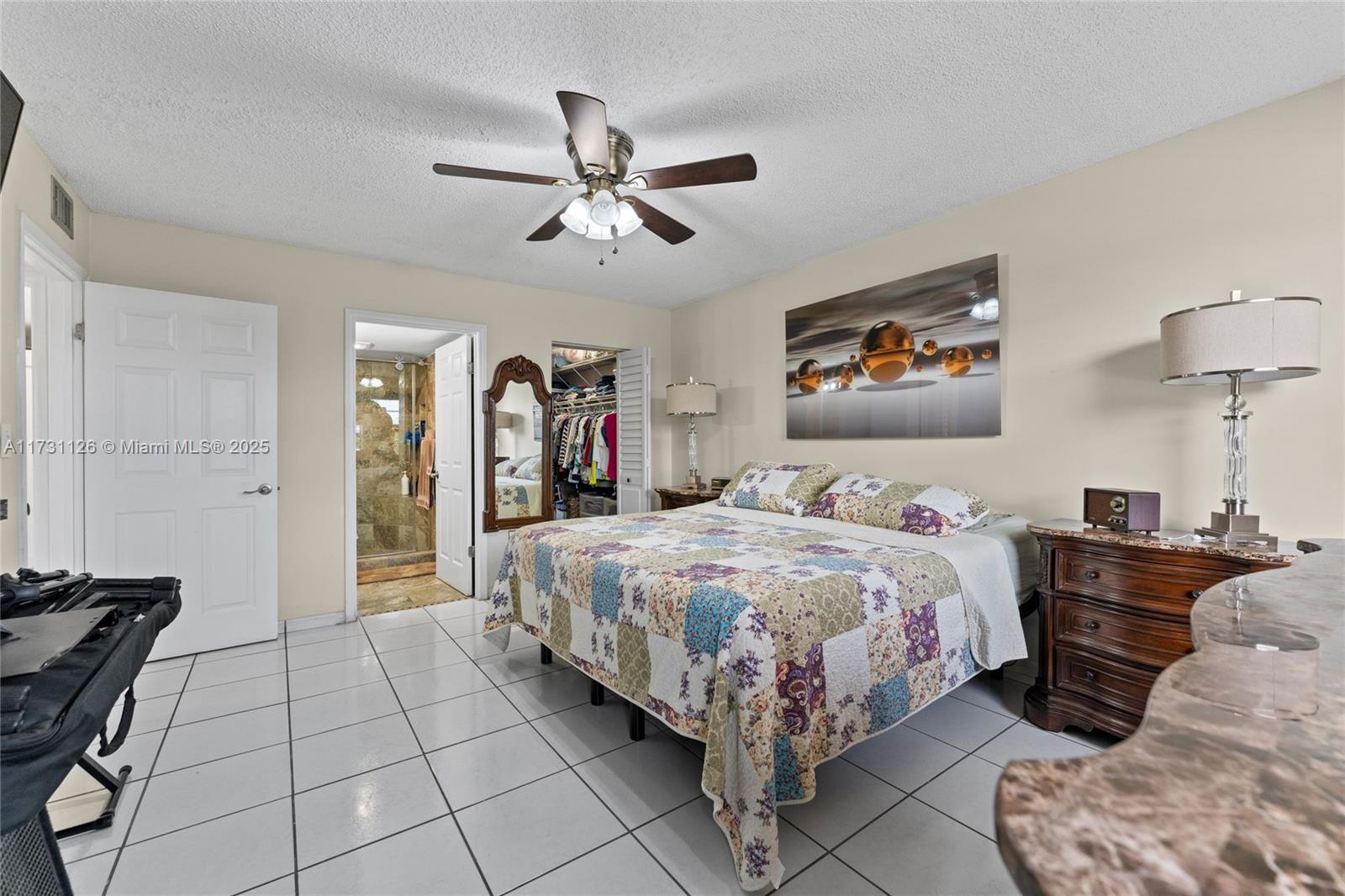 A bedroom features a patchwork quilt on the bed, tiled floors, and an attached bathroom — 605 NW 72nd Ave # 406, Miami FL 33126, MIAMI, FL