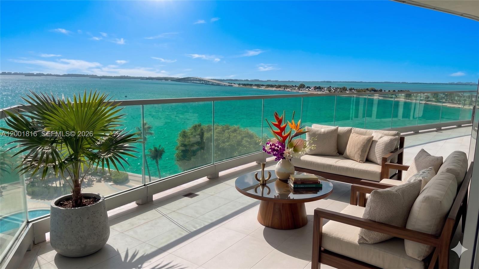 A balcony with outdoor furniture and a potted palm overlooks the ocean and a bridge — 175 SE 25 RD # 504, Miami FL 33129, MIAMI, FL