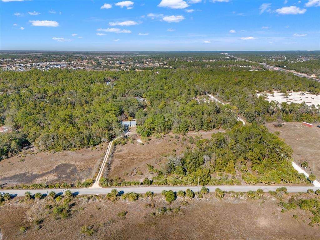 An aerial view shows a house nestled in a wooded lot beside a paved road — 9287 LONG LAKE AVENUE, WEEKI WACHEE, FL