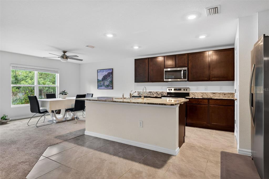 A kitchen with dark wood cabinets, granite countertops, and an island opens to a dining area — 5442 DIANTHA WAY, BROOKSVILLE, FL