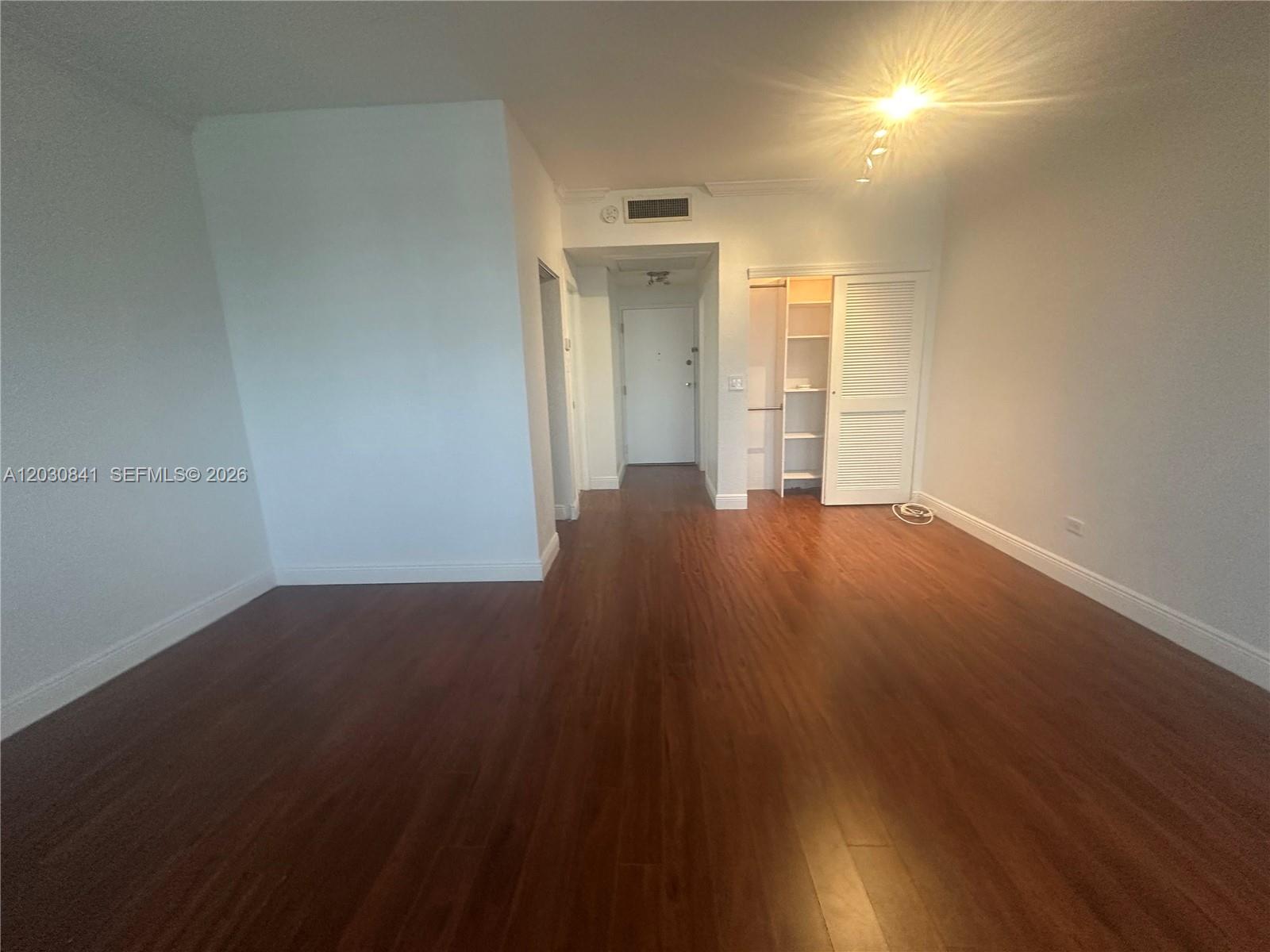 An empty room features dark wood-look flooring, white walls, and a built-in closet — 700 Biltmore Way # 408, Coral Gables FL 33134, CORAL GABLES, FL