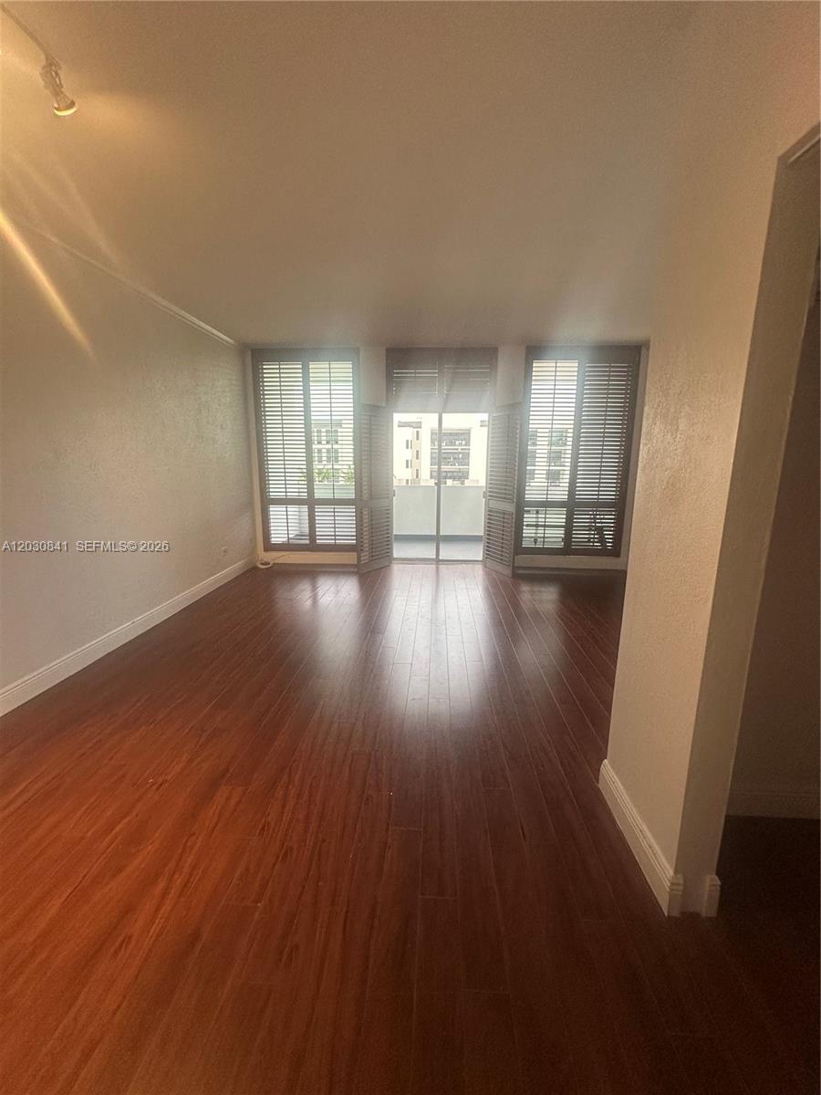 An empty room features dark wood-look flooring, light-colored walls, and a balcony with shutters — 700 Biltmore Way # 408, Coral Gables FL 33134, CORAL GABLES, FL