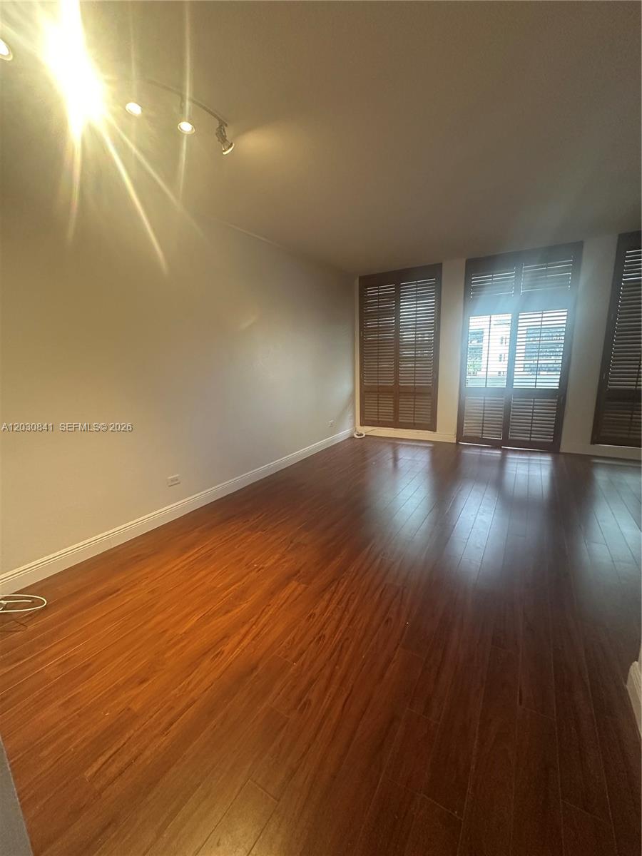 An empty room features dark wood flooring, white walls, and large windows with wooden shutters — 700 Biltmore Way # 408, Coral Gables FL 33134, CORAL GABLES, FL