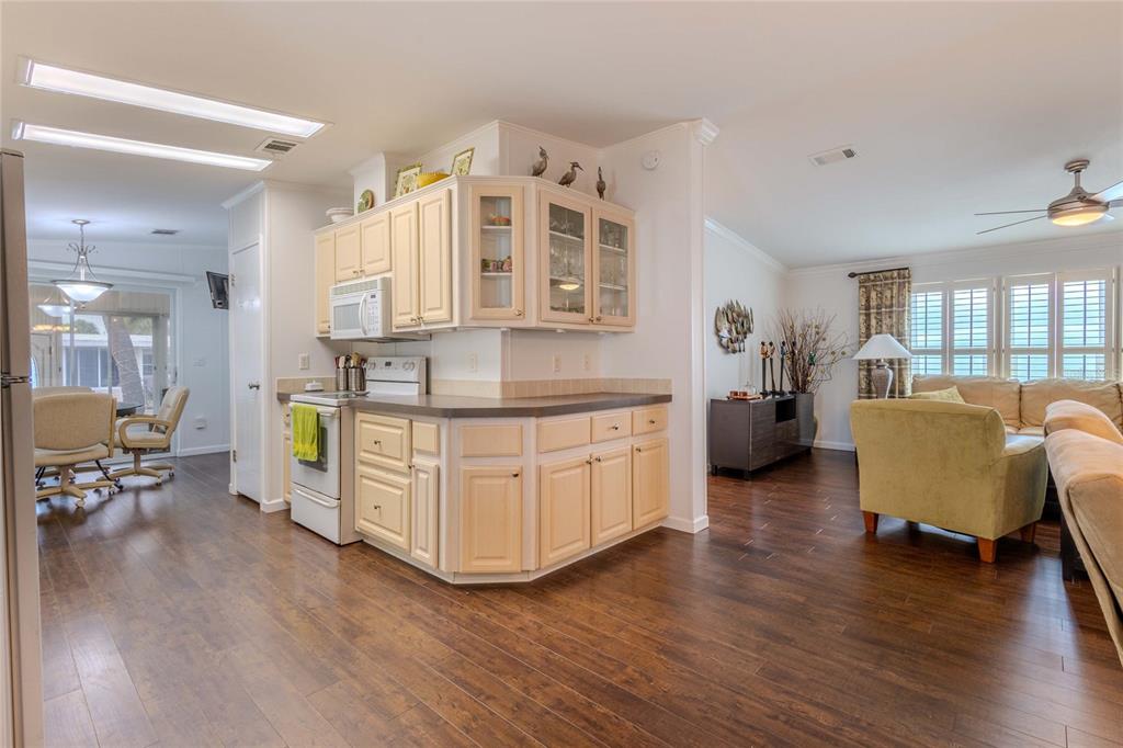 A kitchen with light-colored cabinets and dark countertops opens into a living area with wood floors — 2100 KINGS HIGHWAY UNIT 529, PORT CHARLOTTE, FL
