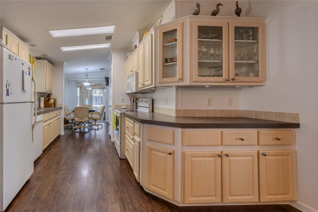 A kitchen features light wood cabinets, dark countertops, and wood-look flooring leading to a dining area — 2100 KINGS HIGHWAY UNIT 529, PORT CHARLOTTE, FL