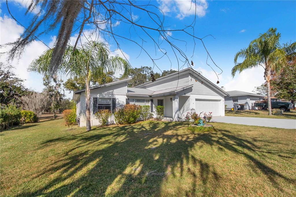 A single-story house with light gray siding, a garage, and palm trees in the yard — 3 MAPLE RUN, HAINES CITY, FL