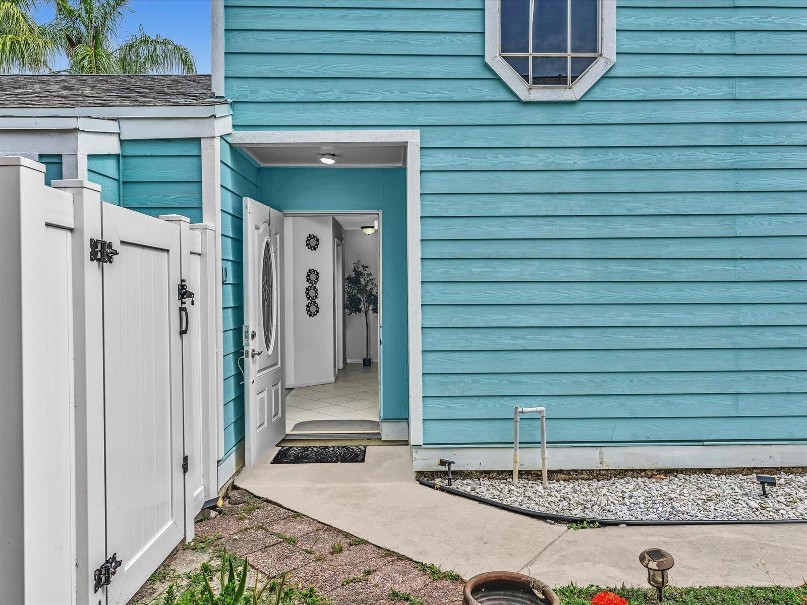 The exterior of a blue house features a white fence, a walkway, and an open door — 5610 Dewberry Way, West Palm Beach FL 33415, WEST PALM BEACH, FL