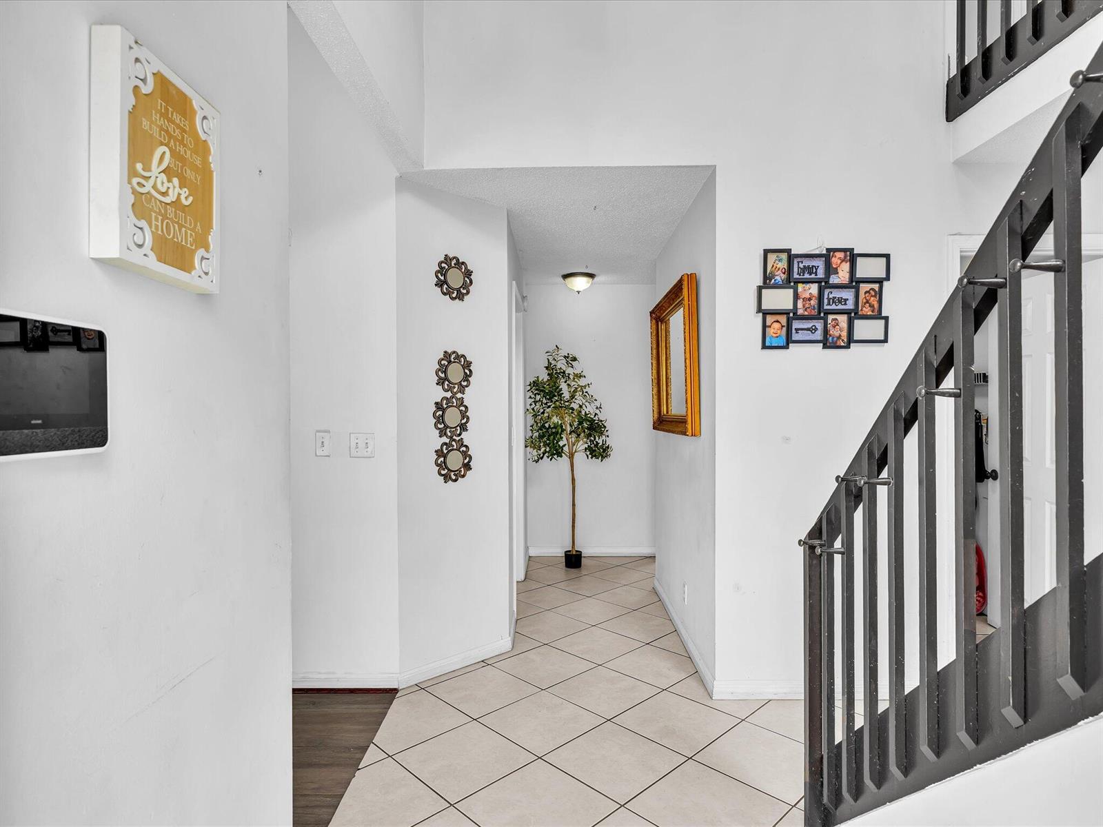 An entryway features a tiled floor, a staircase with dark railings, and wall-mounted decor — 5610 Dewberry Way, West Palm Beach FL 33415, WEST PALM BEACH, FL