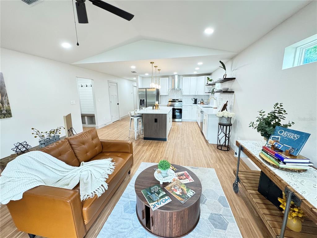 An open-concept living room and kitchen featuring a leather sofa, wood flooring, and white cabinetry — 823 NW 13TH AVENUE, OCALA, FL