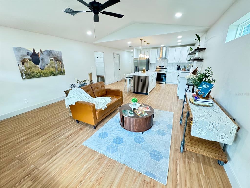 An open-concept living room and kitchen featuring wood-look flooring, a leather sofa, and a kitchen island — 823 NW 13TH AVENUE, OCALA, FL