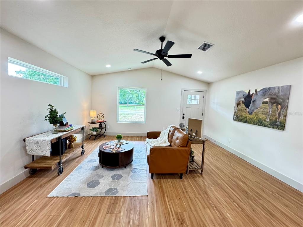 A living room features light wood-look flooring, a brown leather sofa, and a ceiling fan — 823 NW 13TH AVENUE, OCALA, FL
